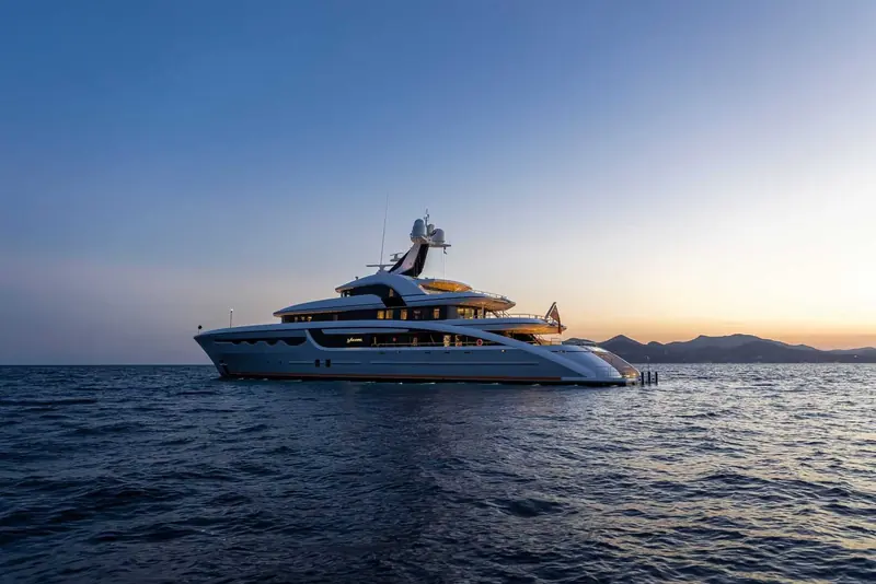 Soaring at anchor at sunset, her low sport-yacht profile set against a darkening headland.