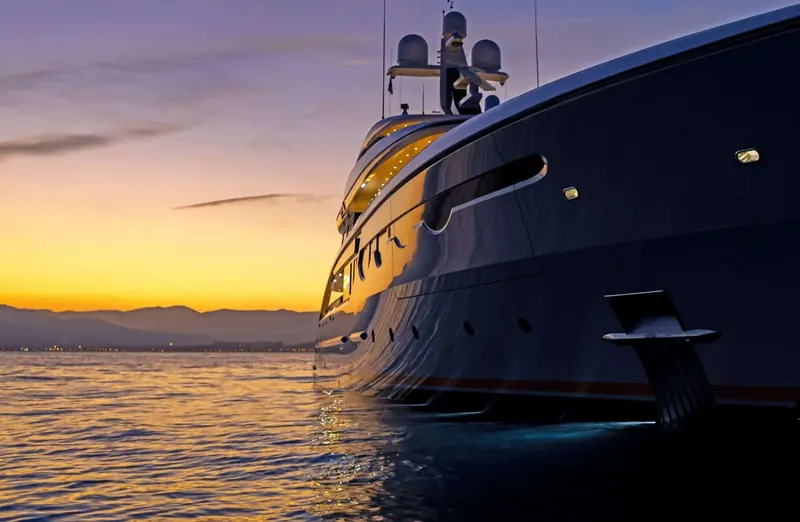 The bow at sunset, orange light catching the topsides as she swings at anchor.