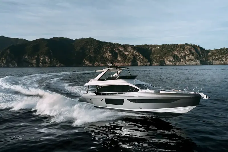 Under way at speed off a wooded headland, throwing a wide, aerated wake typical of a planing hull in the high-50-tonne range.