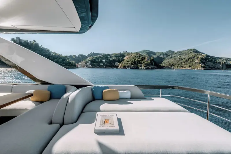 Flybridge lounge seating open on three sides, cushioned in pale grey with mustard and blue accent pillows.