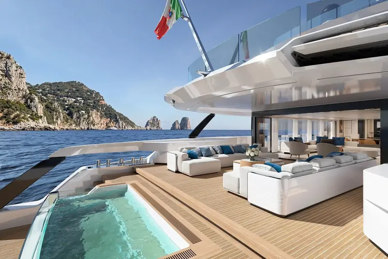 The aft deck jacuzzi and lounge, glass-sided so bathers keep the view of the Faraglioni rather than looking at teak, with the salon opening directly onto the same deck through full-height glazing.