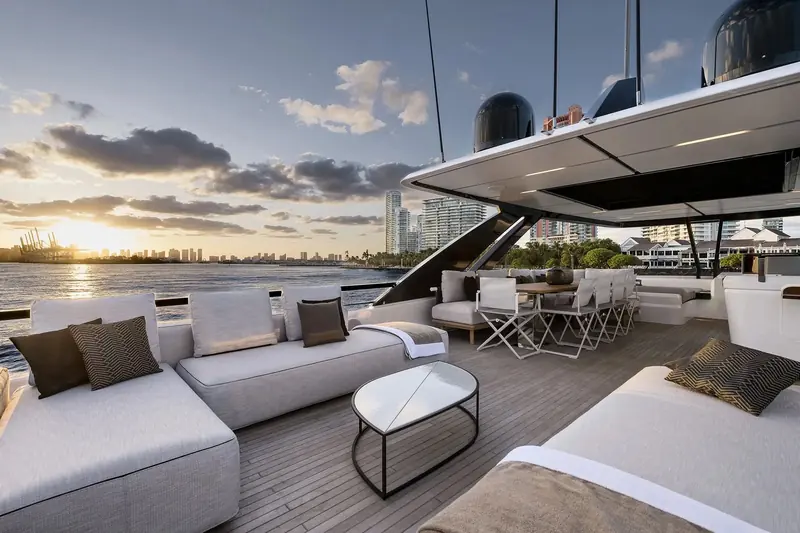 The flybridge dining and lounge area at dusk in Miami, with the hardtop's retractable roof panels open and the port's cranes visible across the water.