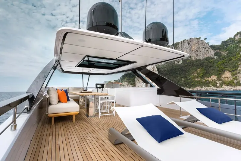 Twin sunpads on the flybridge sit under the folded hardtop, with the boat's radar arch and antennas overhead and the same Amalfi cliffs behind.