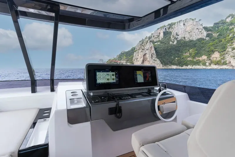 The flybridge helm carries twin multifunction displays and a wheel finished to match the interior joinery, positioned for the skipper to see over the bow at anchor.
