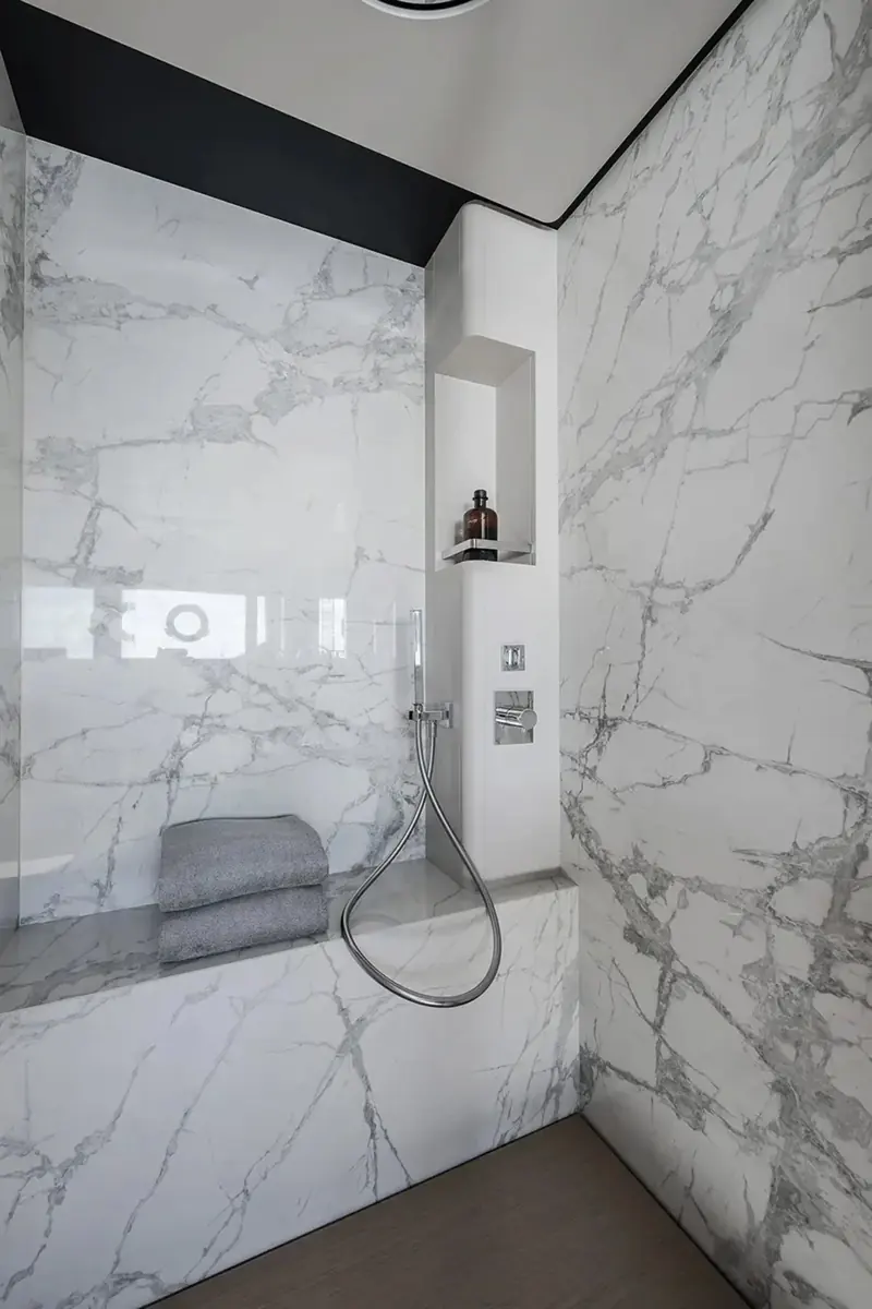 A guest bathroom finished in bookmatched grey-veined marble from floor to ceiling, with a recessed shower niche and chrome fittings.