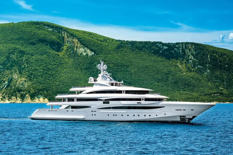 Underway along a green, cliff-backed coastline, her sundeck awning folded down and radar mast raised for open water.