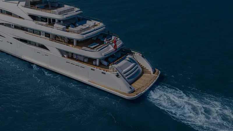 An overhead view of the swim platform and aft deck loungers, with guests visible near the flag staff as she cruises at speed.