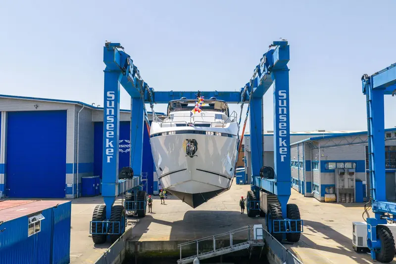A gantry travel hoist, its beams stencilled Sunseeker, carries the hull between the sheds and the slipway - the everyday machinery behind a launch day.