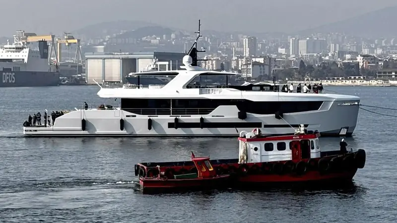 Under tow past the Istanbul waterfront, Aisha's raised pilothouse and open aft deck profile show the volume Red Yacht Design built into a 9.1-metre beam.