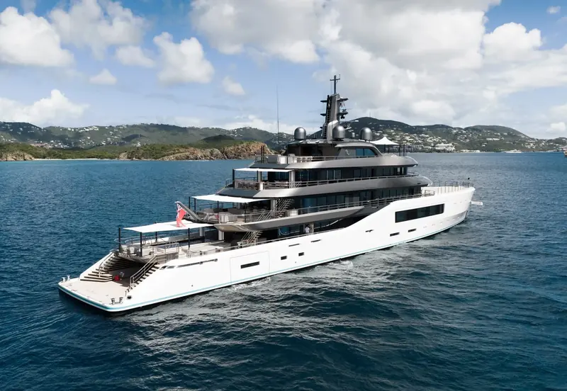 Pangea's superstructure recedes in a long broadside view, the beach club deck and aft pool area visible low against the waterline.