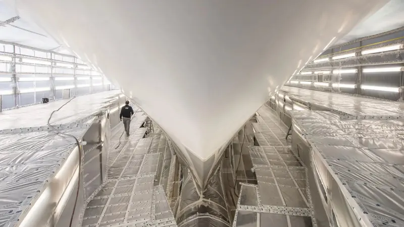 A superyacht's bow inside a covered shed during paintwork, protected from weather and controlled for temperature and humidity.