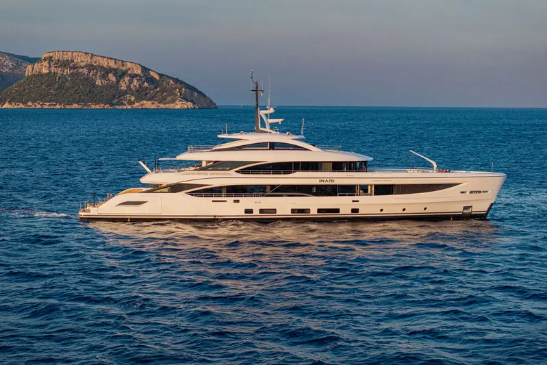 Inari at anchor off a rocky Mediterranean headland, her name lettered on the hull; the 49.9-metre Benetti B.Now 50M is listed for sale at EUR 41,000,000 with Divo Yacht.