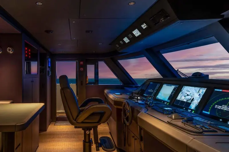 The wheelhouse at dusk: multi-function displays and autopilot controls framed by the bridge's wraparound glass.