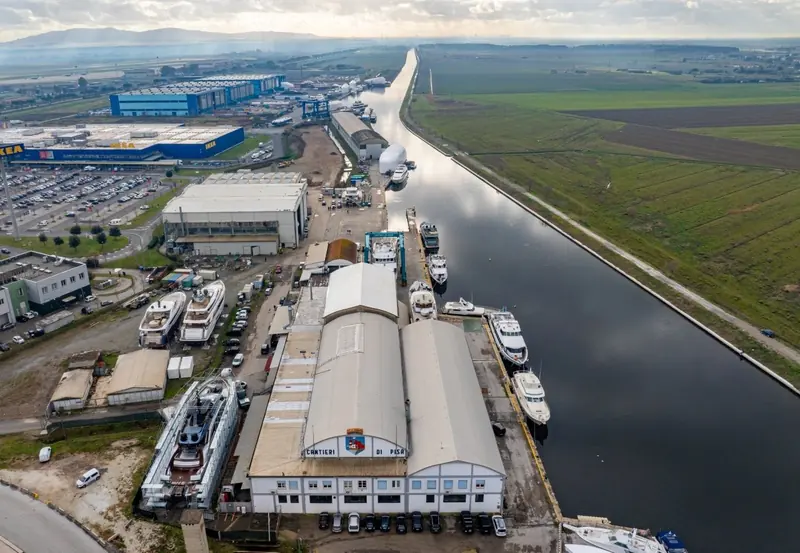 An aerial view of the Cantieri di Pisa shipyard on the Arno canal at Marina di Pisa, with hauled-out yachts alongside the sheds.