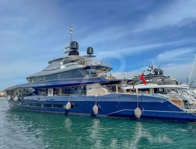 Queen Yaz moored among sailing yachts. Her navy-blue hull and displacement form favour range and comfort over outright speed.