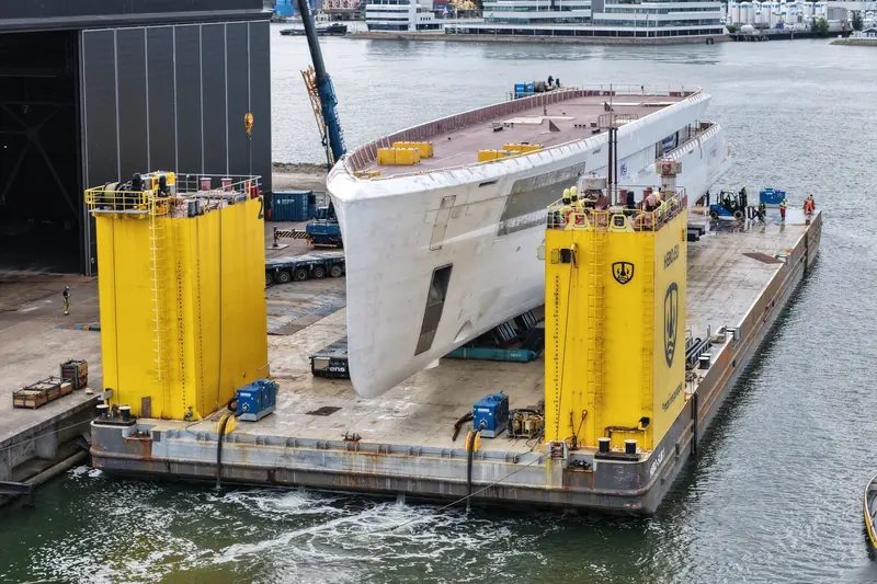 Bow-on, showing the hull's raked stem and the yellow jacking towers used to lift her onto the barge.