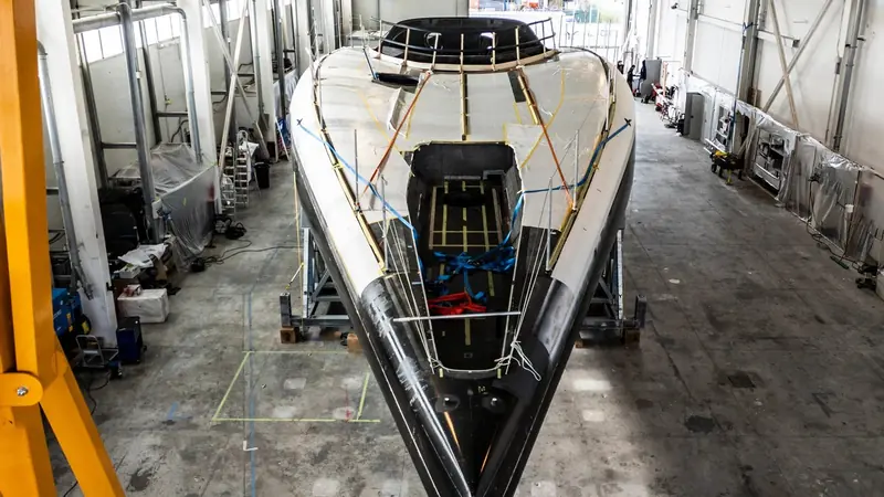 A bow-on view of the same hull on its cradle, showing the deep, narrow forward sections and the taped seams still awaiting fairing before paint.