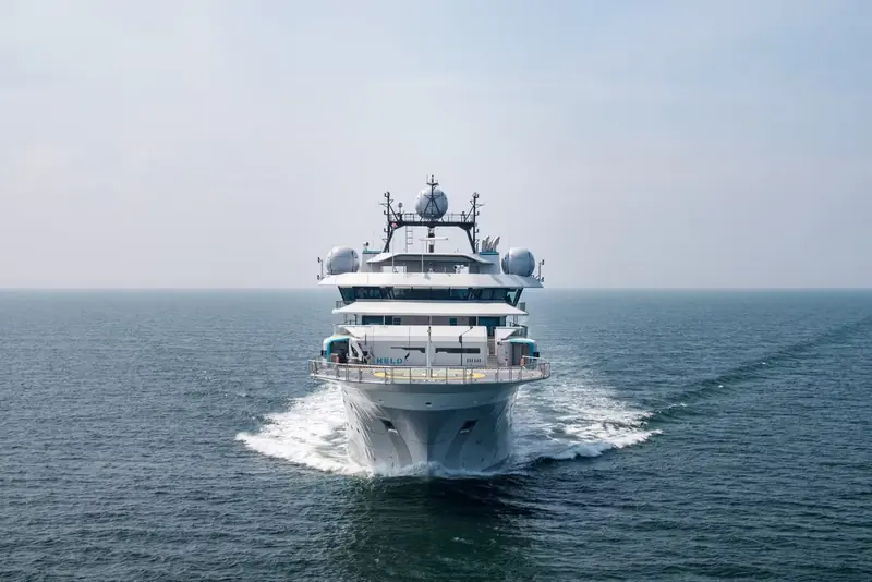 OceanXplorer runs bow-on into a calm sea, her twin satellite domes and enclosed bridge visible above a low grey hull built for open-ocean research.