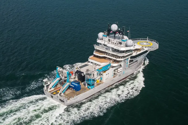 OceanXplorer underway with her yellow-liveried crane and submersible-handling gear visible on the aft working deck, alongside the helideck used for ship-to-shore transfers.