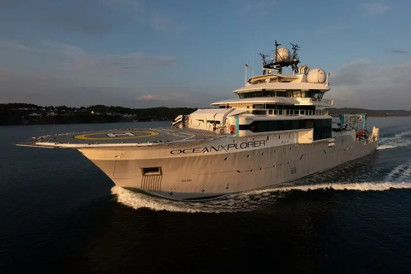 OceanXplorer's flank at dusk, her name lit along the hull above the helideck, the silhouette that has carried the studio's exterior styling into BBC's Blue Planet.