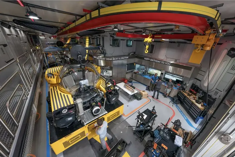Inside OceanXplorer's mission bay, a yellow overhead crane and a submersible sit under working lights, the kind of interior arrangement the design team built into the vessel's brief.