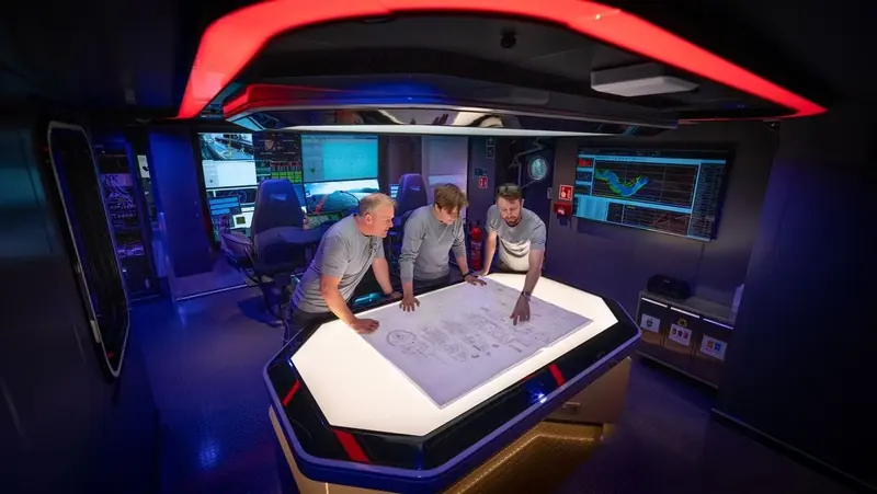 Crew gather around a lit chart table in OceanXplorer's mission control room, the red-rimmed command space that became one of the vessel's signature interiors.