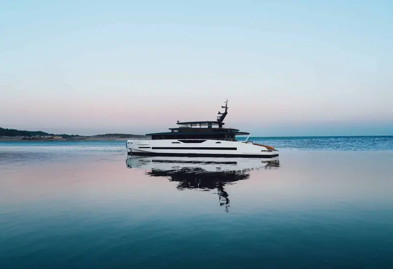 Merinos sits at anchor at dusk, her low-profile solar superstructure visible along the flybridge.
