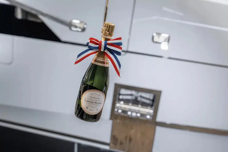 The bottle at the naming. She is the second Heesen for the same owners, who the yard describes as returning clients rather than first-time buyers.