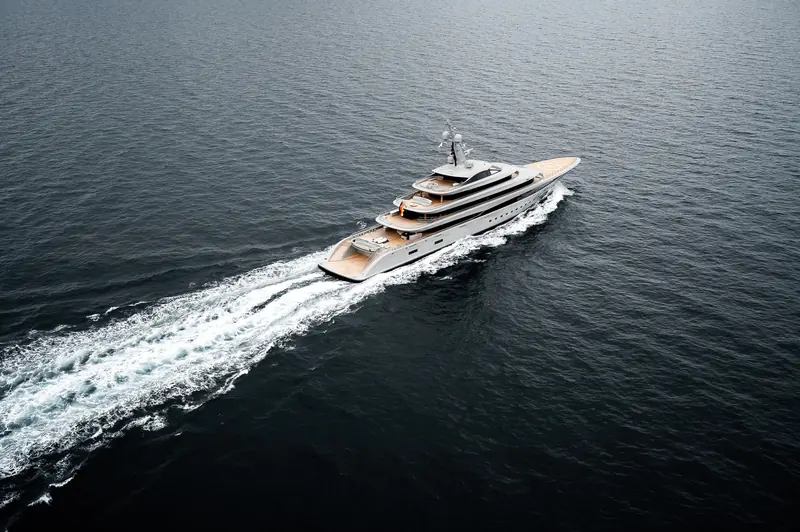 An aerial three-quarter view shows the full deck plan: helipad forward, open sundeck, and the tender garage aft where the beach club sits below.