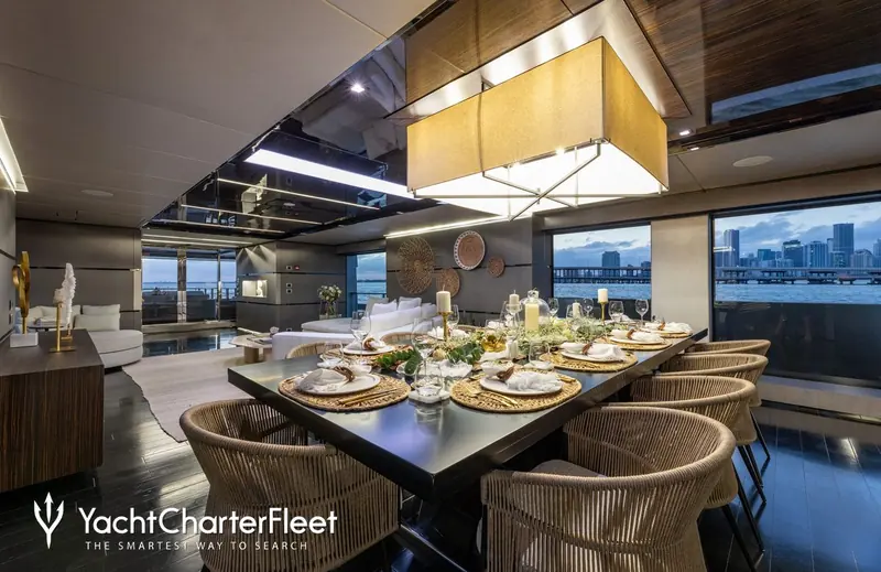 The dining table and salon at dusk, with Miami's skyline through the windows. Five cabins sleep 11 guests across a tri-deck layout by Admiral Centro Stile.