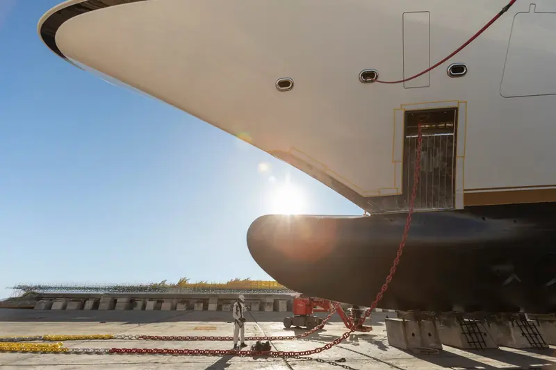 A yacht's bow overhangs the hardstanding in low winter light, the kind of tight, high-value refit work the yard's expansion is designed to accommodate without losing capacity elsewhere.