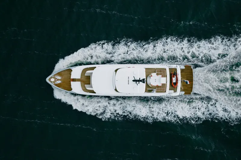 Straight overhead, showing the full deck plan: teak side decks, the tender and jet-ski stowed aft, and the IMO number stencilled into the foredeck.