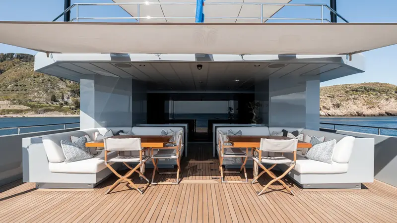 The sundeck's twin alfresco dining tables, shaded under a fixed hardtop and soft awning. Moonshot carries her entertaining space on the deck above the saloon rather than folding it into the main deck aft.