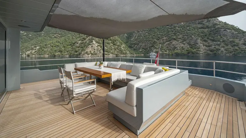 Cockpit dining aft, awning down, at anchor in a quiet Turkish bay. This is the cruising ground Moonshot was built for: shallow draft, a wood hull and a modest 3,000nm range suited to the Aegean and the Med, not an ocean crossing.