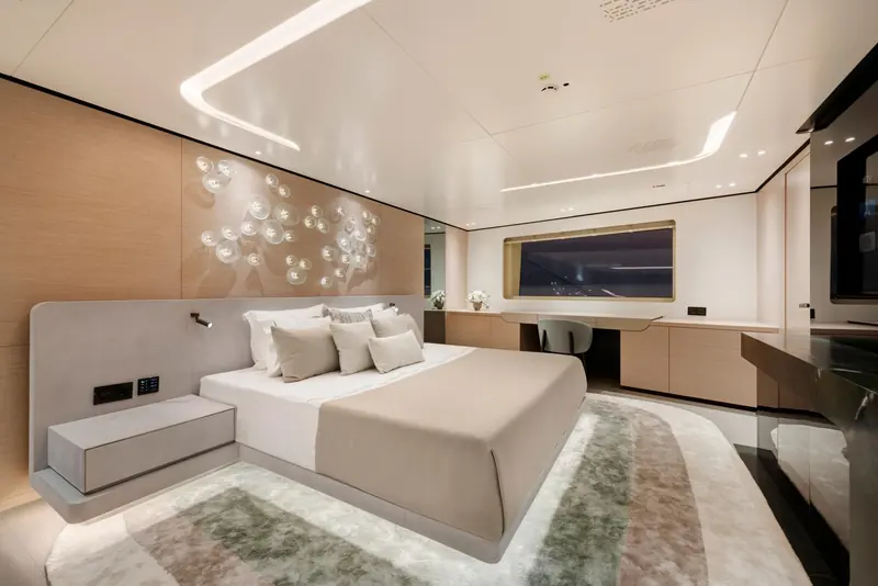 The owner's suite forward on the main deck, finished by Minotti in oak and grey upholstery, with a private desk and a full-beam window.