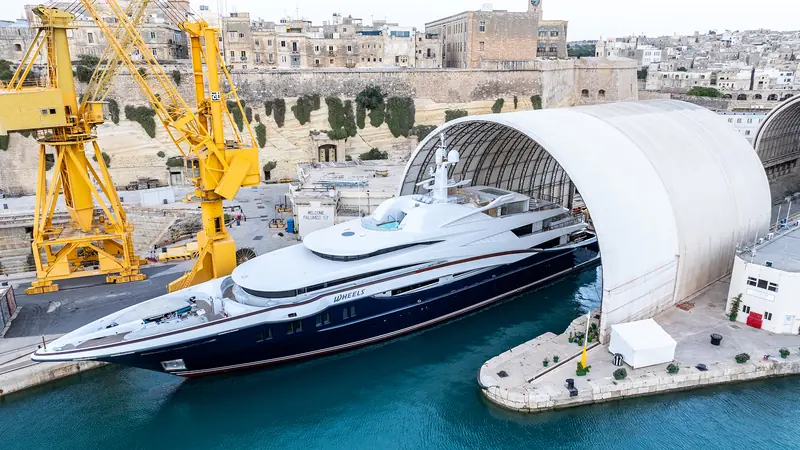 M/Y Wheels docked half inside Palumbo SY's covered shed at Malta's Grand Harbour, Valletta's fortifications behind - the network's largest sheds can enclose a yacht for weather-independent work.
