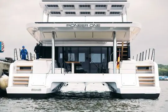 The stern of Pioneer One, her name on the aft bulkhead and the coachroof solar array visible above the swim platforms.