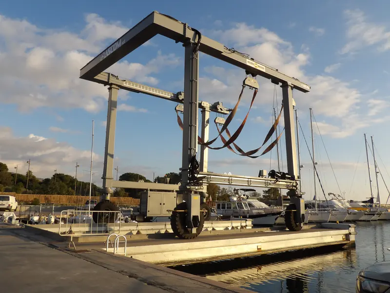 The haul-out itself is billed separately from the surveyor's fee, typically EUR 2,000 to 8,000 depending on size and yard. A travel lift at Marina di Capitana, Sardinia.