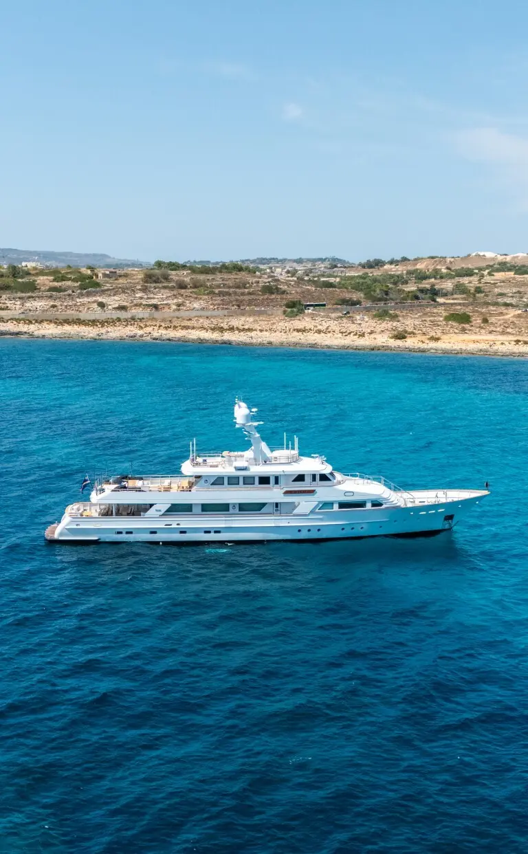 At anchor over shallow turquoise water, Alaia's full-beam owner's suite windows and Beach House aft deck are visible amidships.