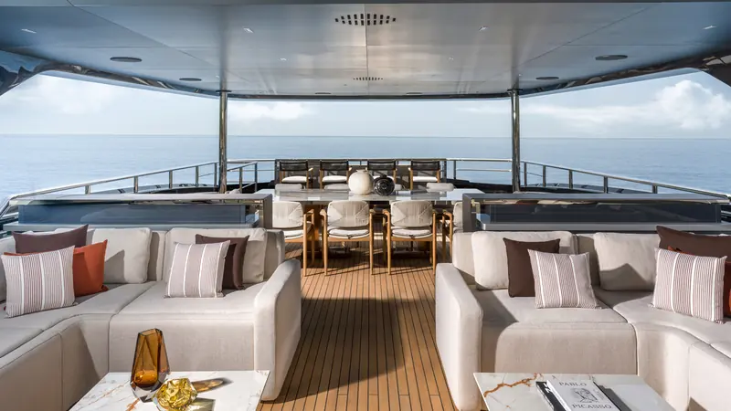 The aft lounge, sheltered under a hardtop, with sofas and dining for ten. Four electric Naiad stabiliser fins keep her steady here without the noise of a hydraulic system.