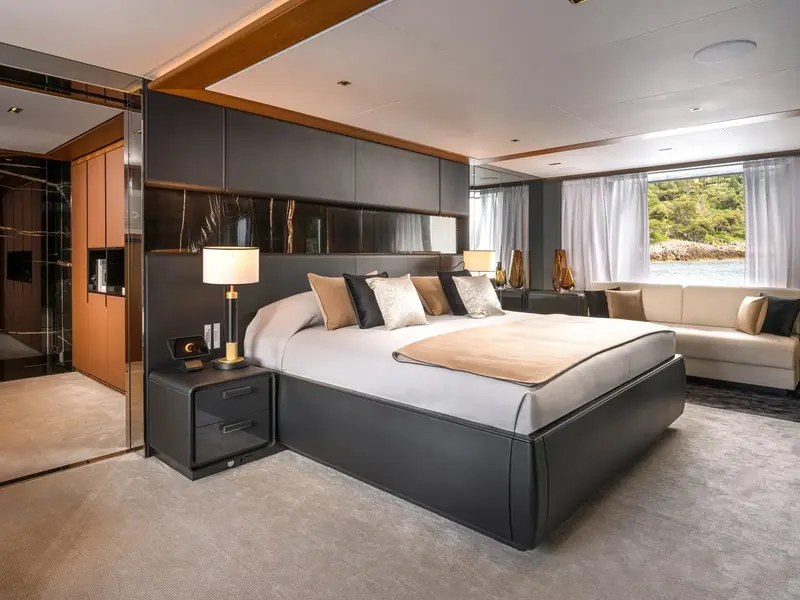 One of the five staterooms aboard Sairu, finished in dark leather panelling with a full-height window onto the anchorage.