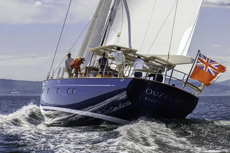 Ouzel's transom, hailing port Bloody Bay beneath her name, under sail during 2026 trials in Penobscot Bay - the Red Ensign marks her as Cayman Islands-flagged.