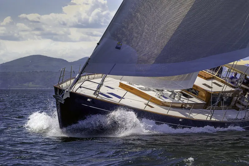 Close on the bow wave under sail, the dark blue hull throwing spray clear over the rail.