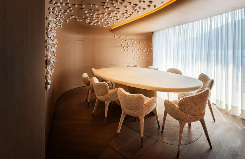 The main-deck dining room, with an oval table, shell-like chairs and a relief of small pale forms across the wall.