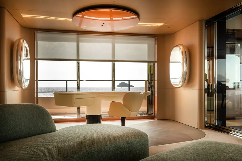 A sitting area with a sculptural desk, a green sofa and oval windows.