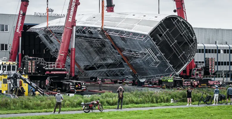 Project 410's hull suspended between two Mammoet cranes over the canal outside Royal Huisman's Vollenhove yard on 25 July 2024, the first time the yacht had been seen outside a closed construction hall.