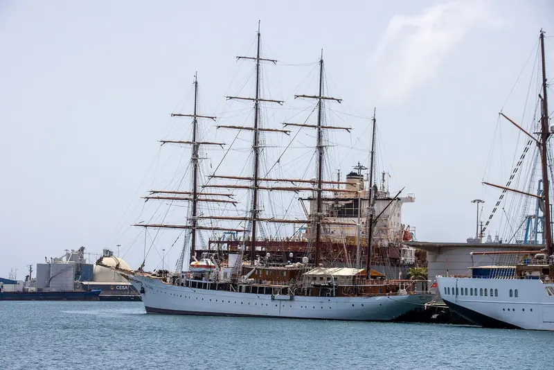 Sea Cloud alongside in Las Palmas, her four masts and the running rigging of a genuine working square-rigger against a container terminal backdrop.