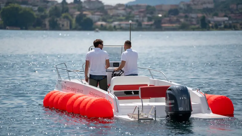 Two crew stand at the helm of a Sea Fend demonstration RIB, its airbags already inflated along both sides of the hull.