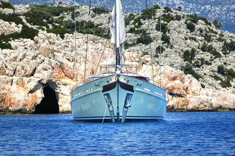 Bow-on at anchor off a limestone coastline. The mainmast stands about 59 metres, the mizzen about 49 metres, carrying roughly 1,400 square metres of sail between them.