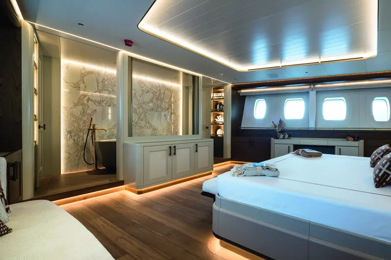 The owner's suite: bed in the foreground, a marble bathroom and freestanding tub beyond, lit by the hull's aircraft-shaped portholes.
